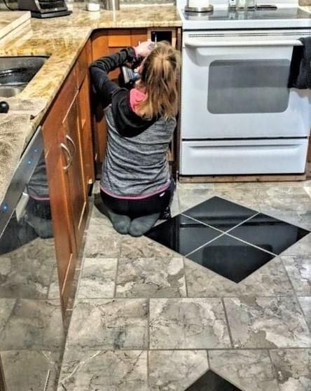 Woman kneeling, working on cabinets in a kitchen, next to a stove.