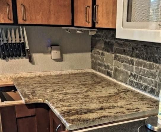 Kitchen countertop with brown granite-like surface, dark wood cabinets, and brick-patterned backsplash.