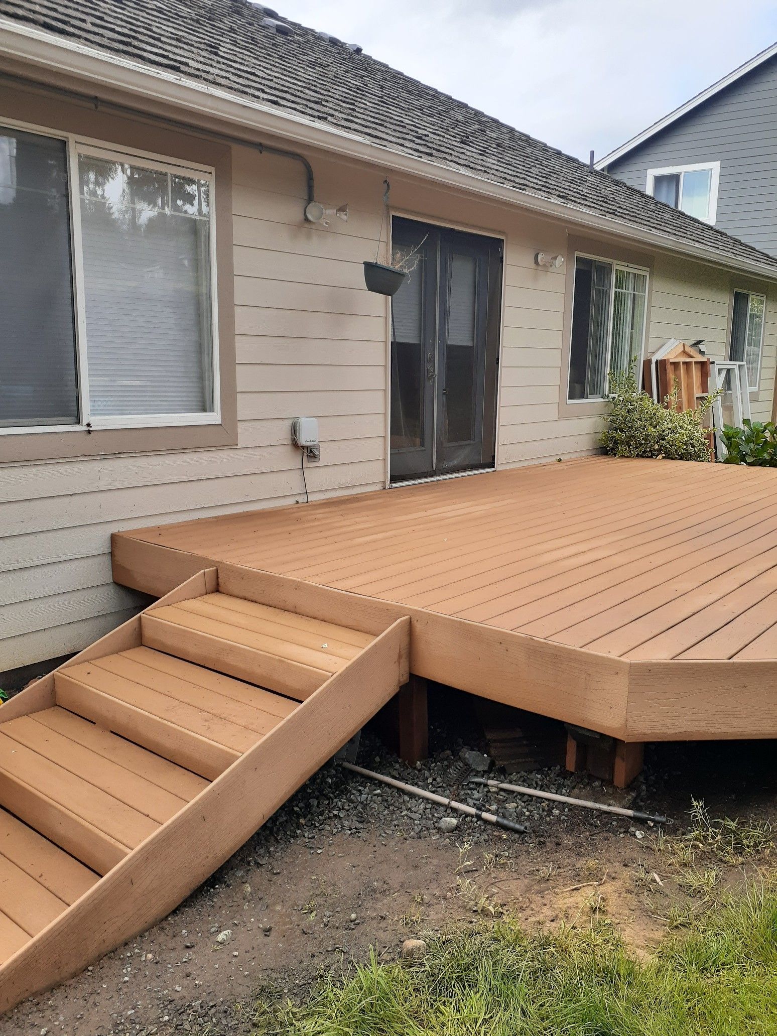 Wooden deck with stairs leading to a beige house with a sliding door and windows.