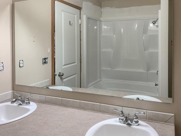 Bathroom with large mirror reflecting sinks, door, and shower.