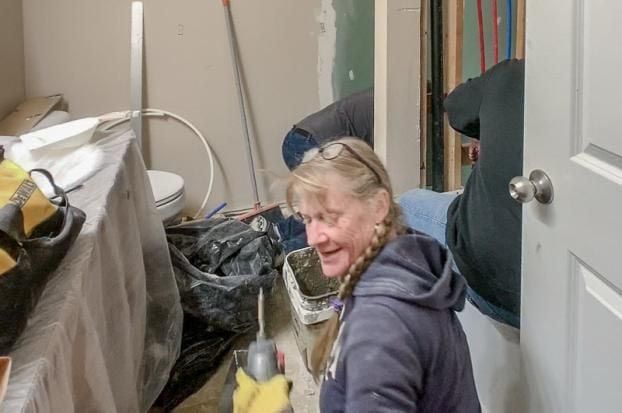 Woman smiling in a room under renovation. Others are working in the background. Tools and materials are scattered around.