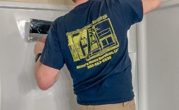 Person in a blue shirt with a company logo installing something on a white shower wall.