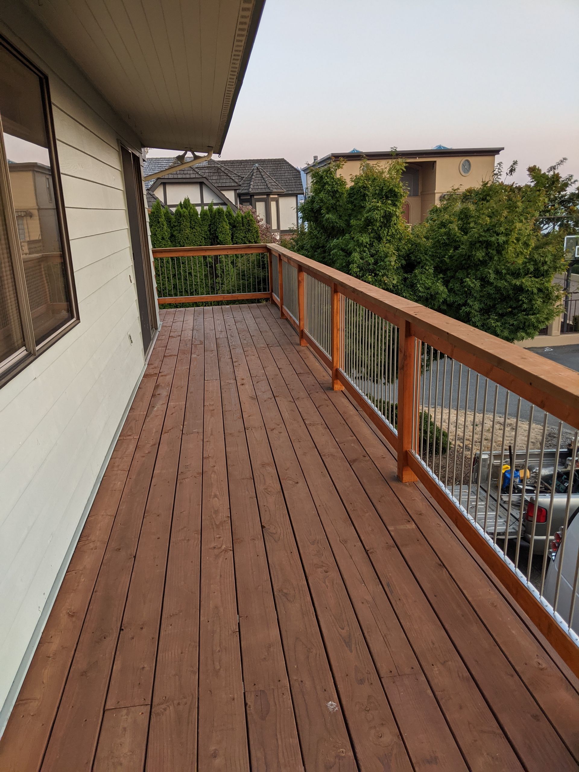 Wooden deck with brown planks and a railing with metal balusters. Building exterior visible.