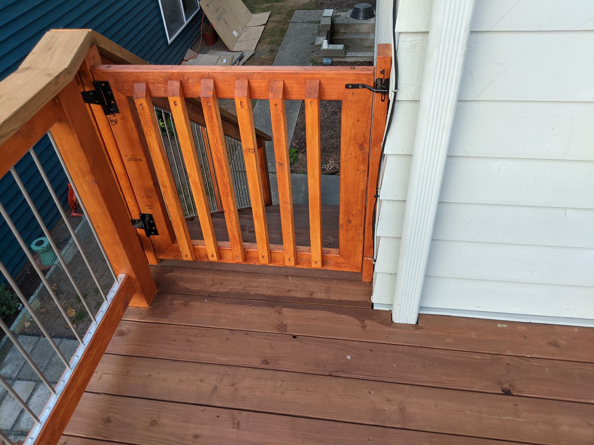 Wooden deck gate, stained brown, installed on a deck. Shows vertical slats and black hinges.