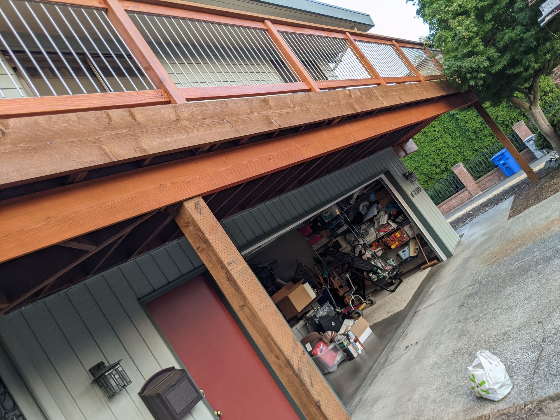 Wooden deck over a garage. Deck has metal railings. Garage door is open, filled with storage items.