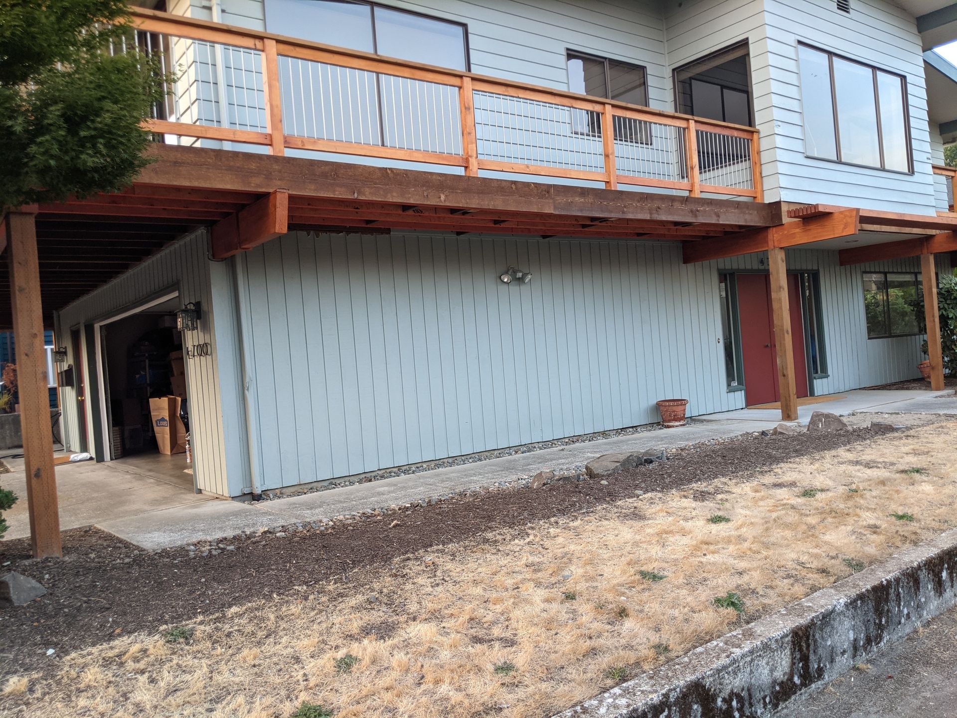 Two-story house with a wooden deck. The ground floor has a garage, light blue siding.