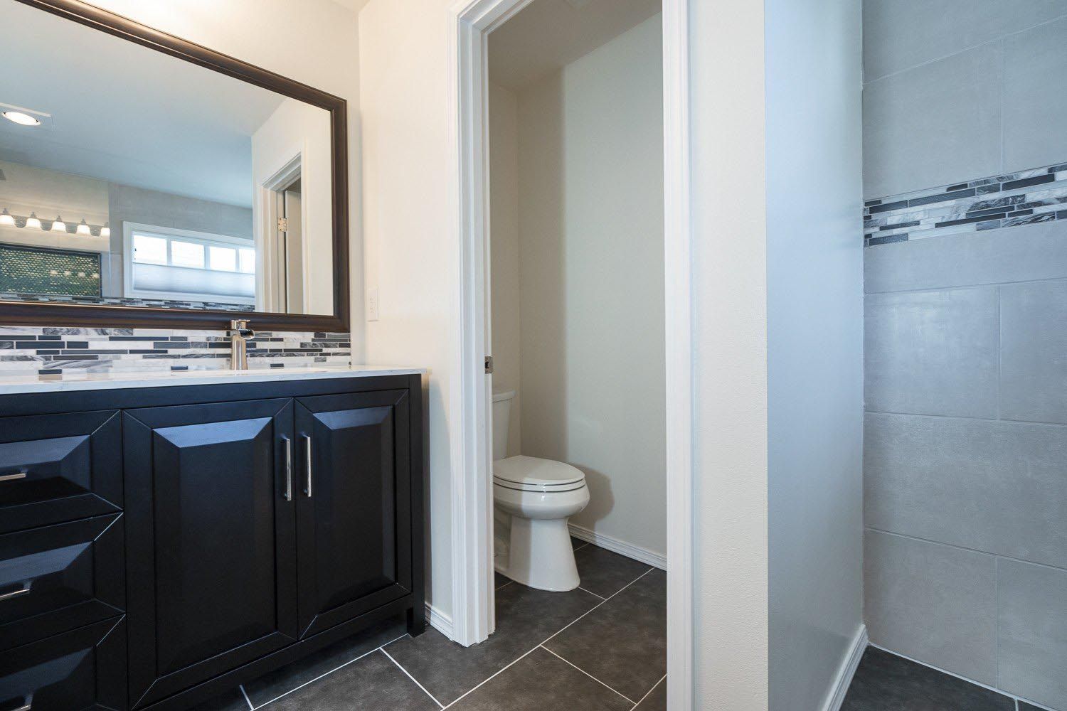 Bathroom with black vanity, white toilet, and gray tiled floor and shower.