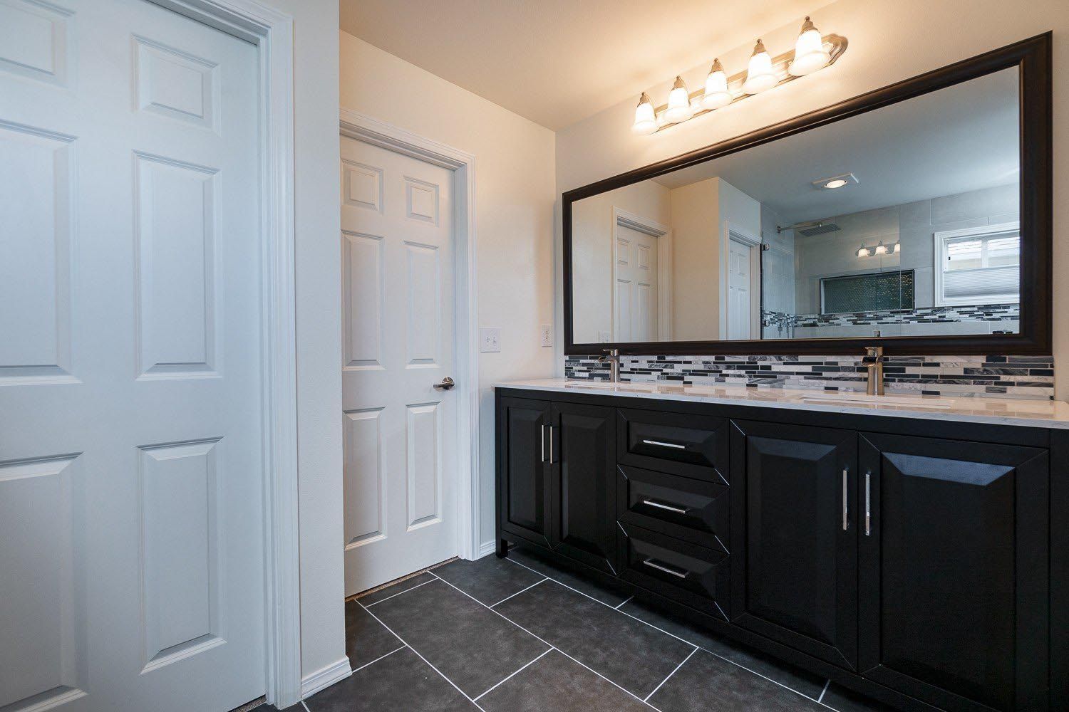 Bathroom with black vanity, large mirror, white doors, and gray tile floor.