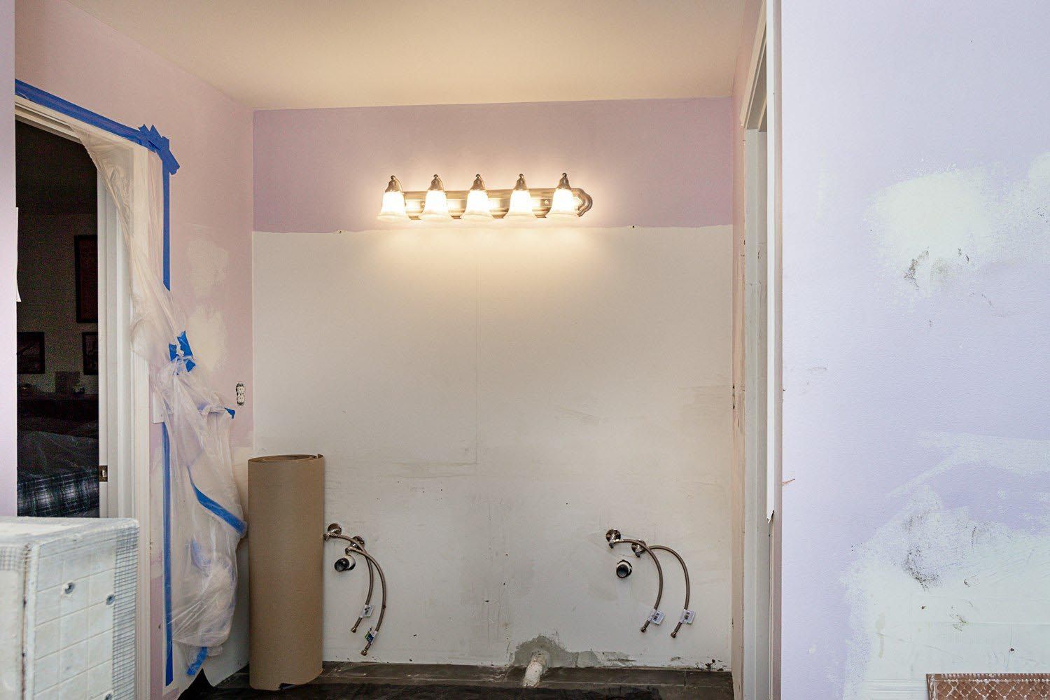 Bathroom renovation: purple and white walls, exposed plumbing, light fixture, roll of paper.