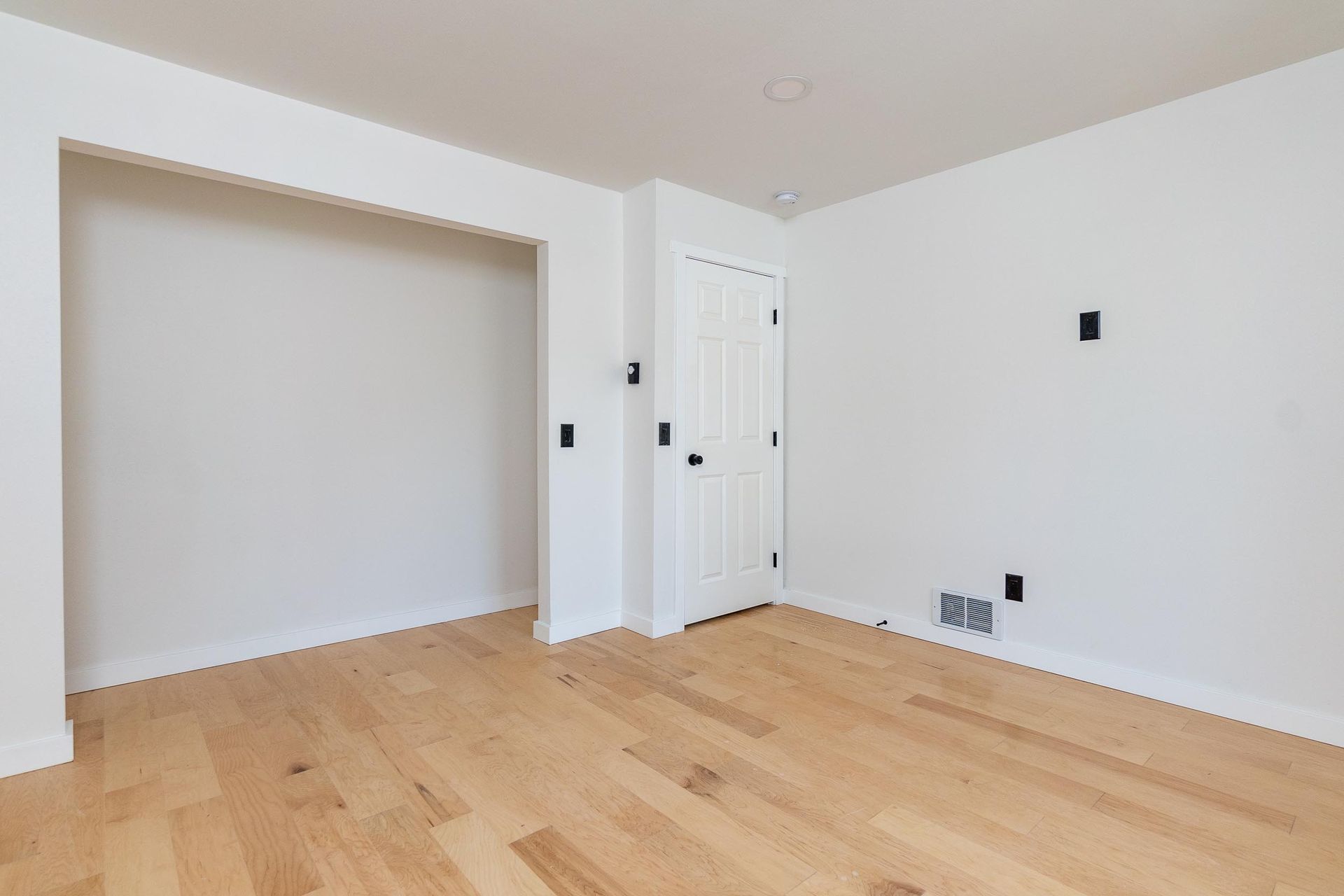 Empty room with hardwood floors, white walls, closet, and a closed door.