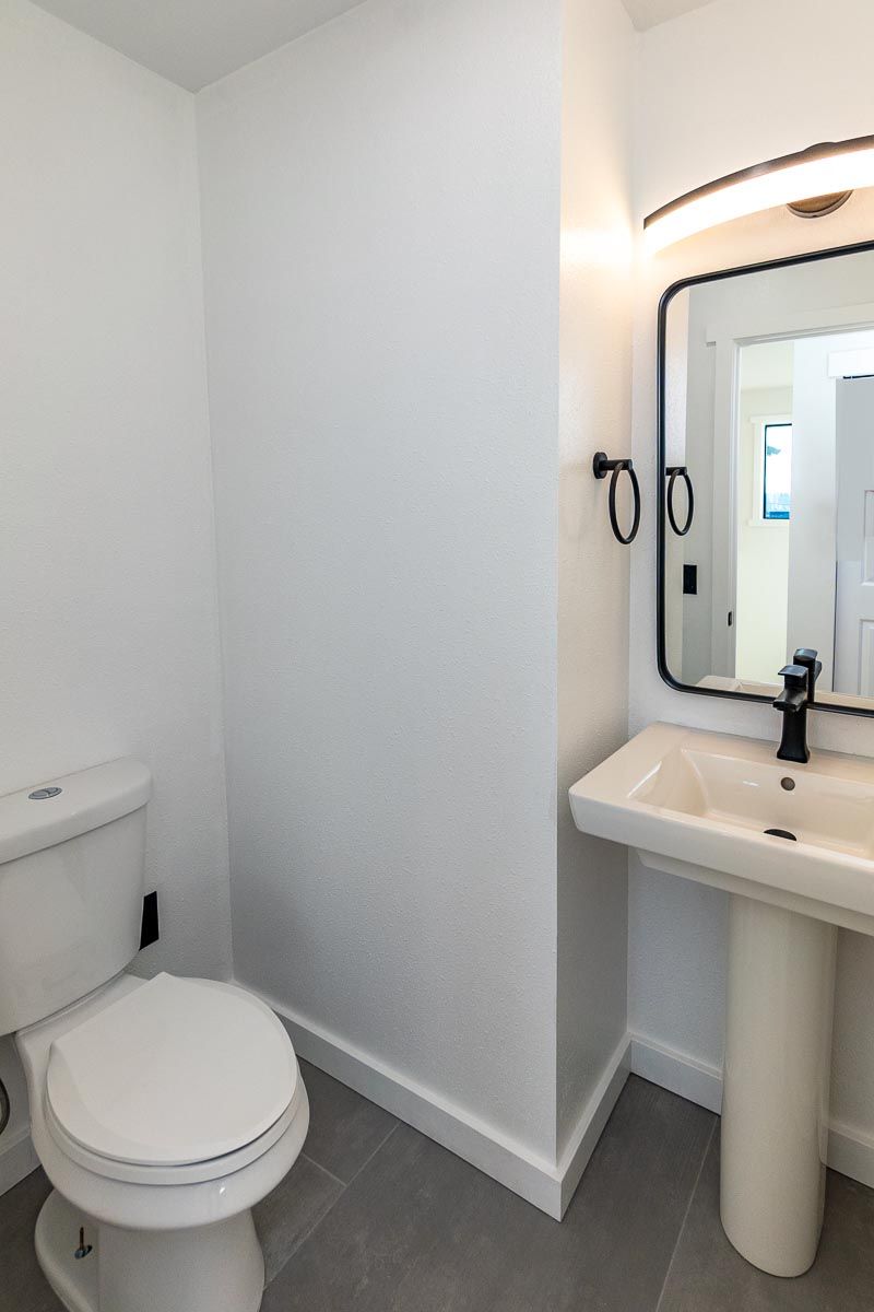 White bathroom with toilet, pedestal sink, mirror, and black fixtures.