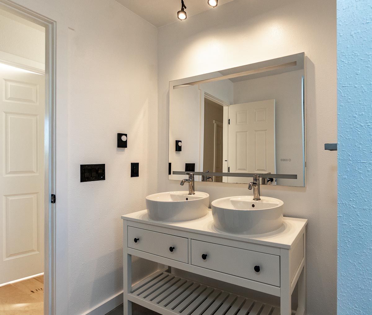 White bathroom with double sinks, large mirror, and open shelving.