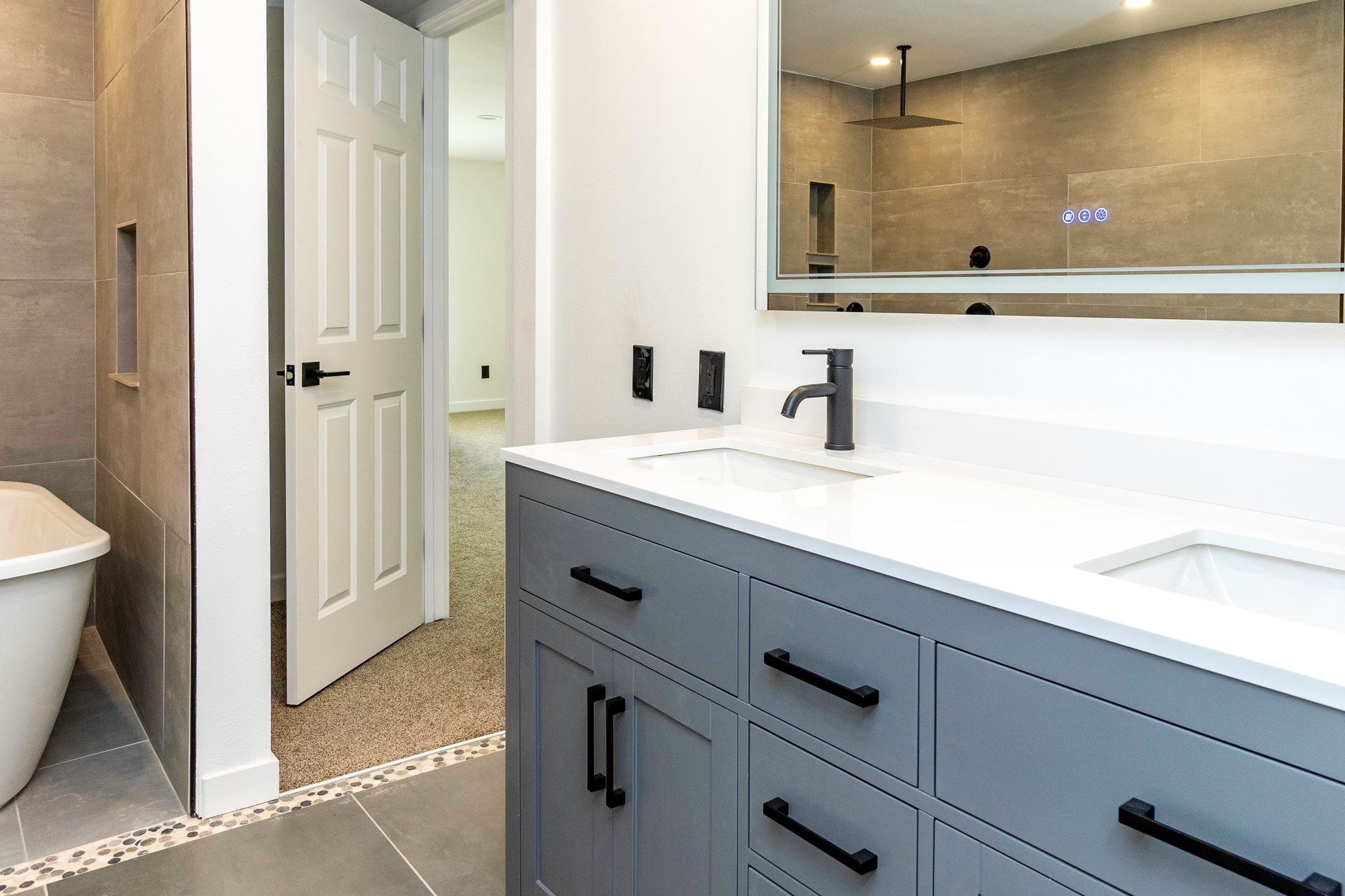 Modern bathroom with gray vanity, white countertop, and large mirror reflecting the shower.
