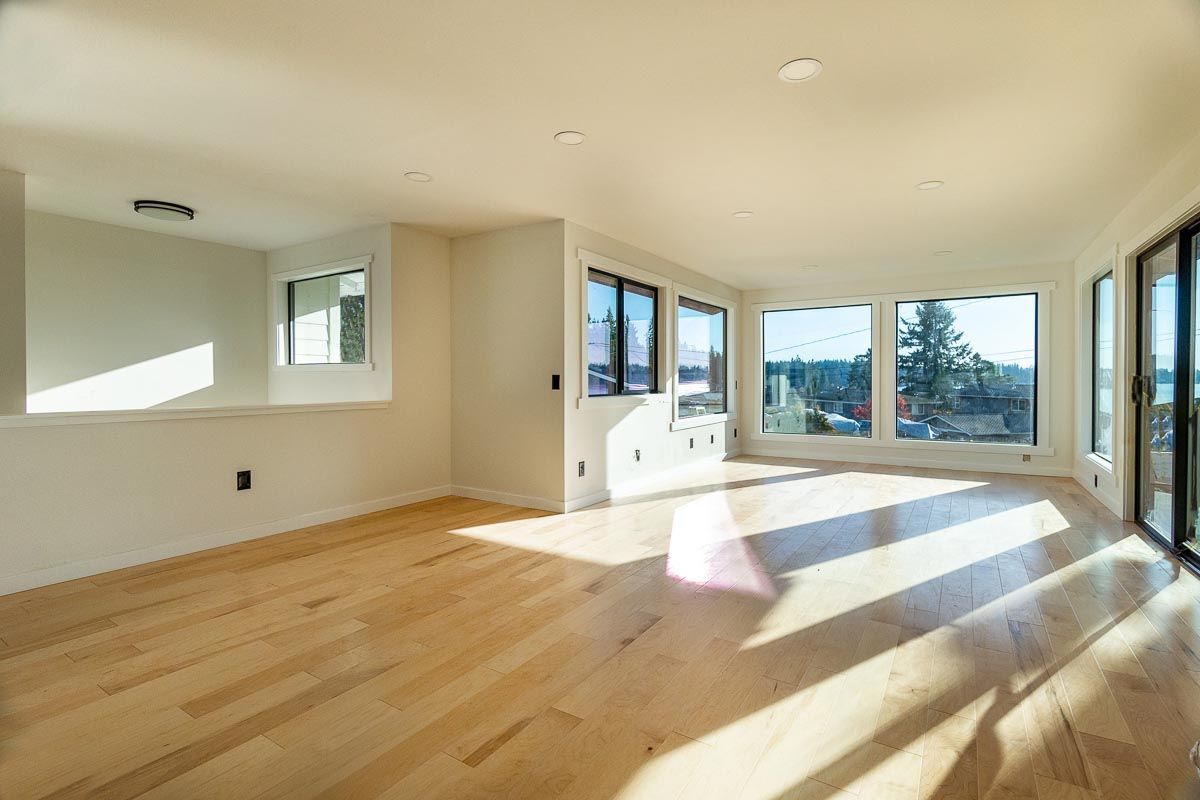 Empty room with light wood floors, many windows, and natural sunlight.