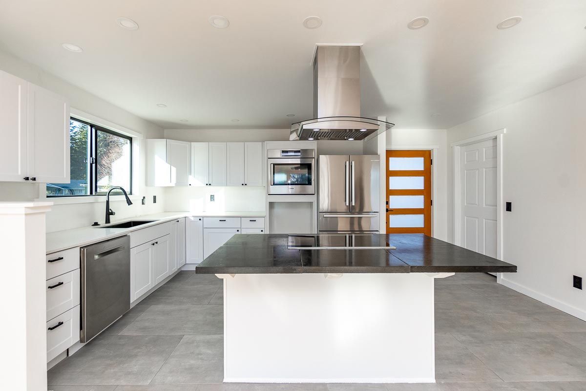 Modern white kitchen with a stainless steel range hood, island, and appliances.