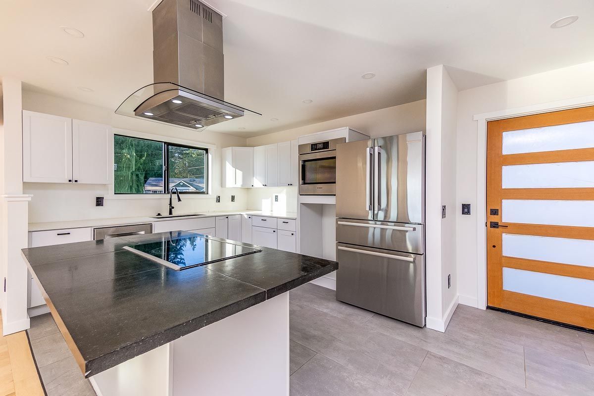 Modern kitchen with white cabinets, stainless steel appliances, and dark island countertop.