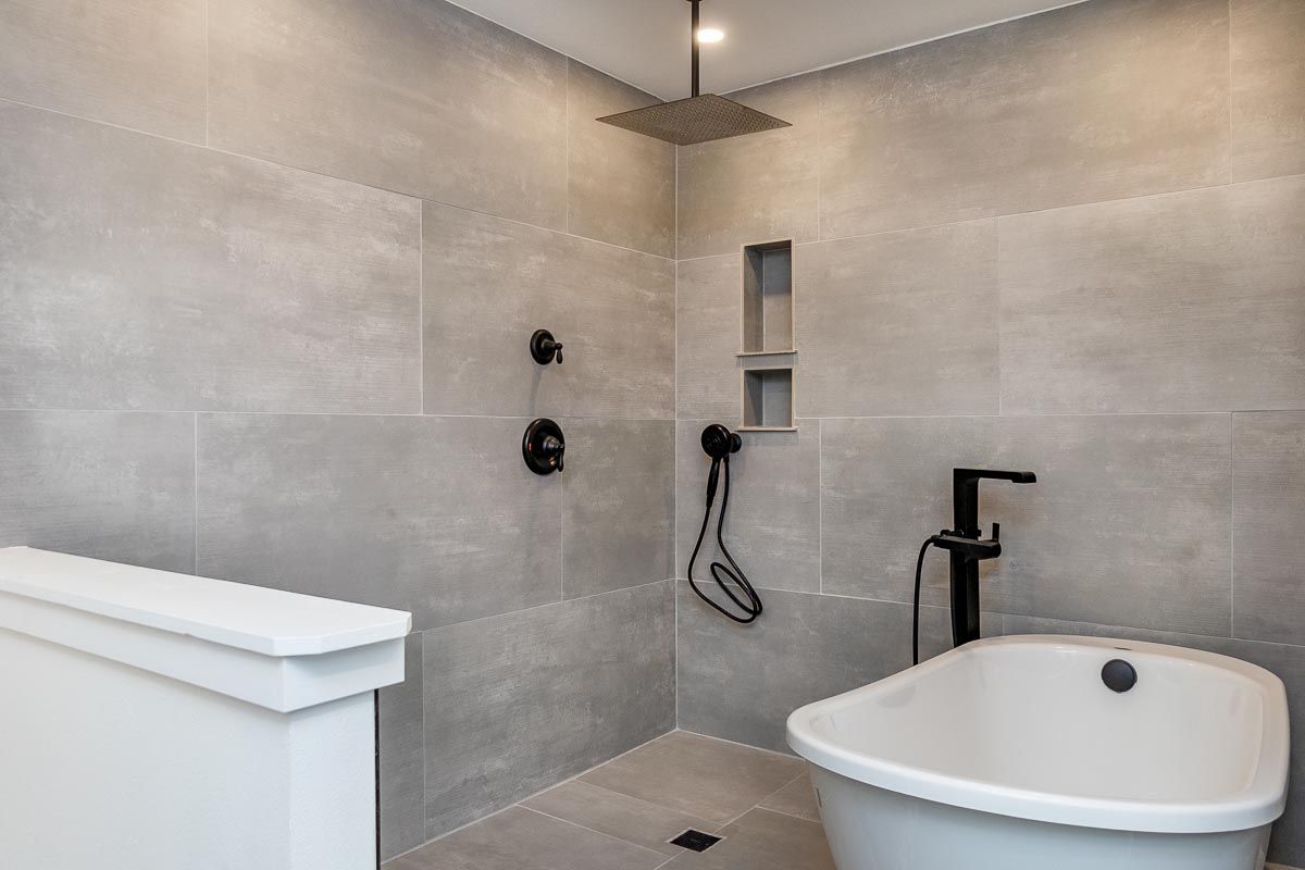 Modern bathroom with gray tiled shower, freestanding tub, black fixtures.