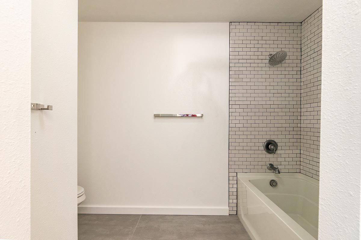 Bathroom with white walls and subway tile shower. Silver towel bars and bathtub.