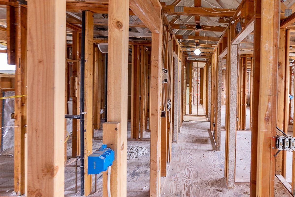 Interior view of a building frame under construction, showing wooden studs, doorways, and unfinished flooring.