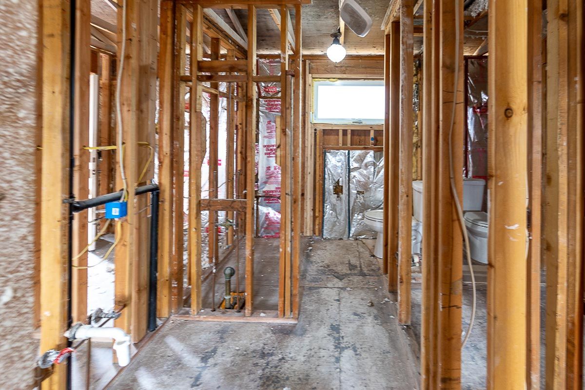 Interior view of a building under construction, showing wooden framing, exposed insulation, and a hallway.