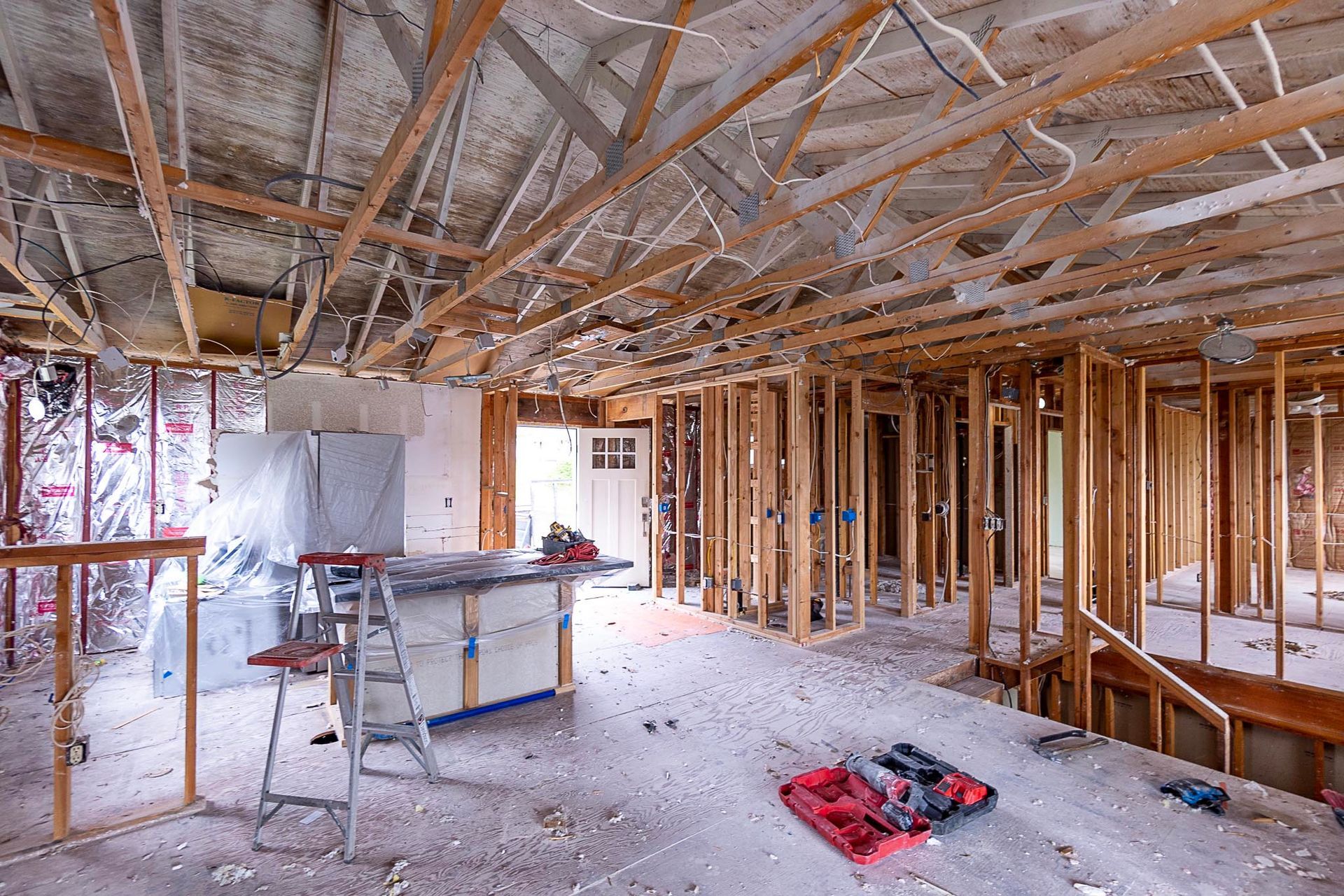 Interior of a building under construction, wooden frames, unfinished ceiling, debris on the floor, and a workbench.