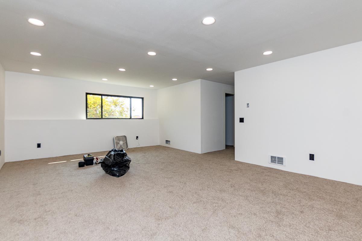 Empty room with white walls, beige carpet, recessed lighting, and a small window.