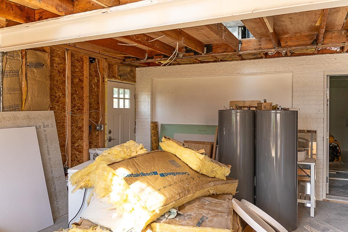 Interior construction site with exposed framing, insulation, water heaters, and a doorway.