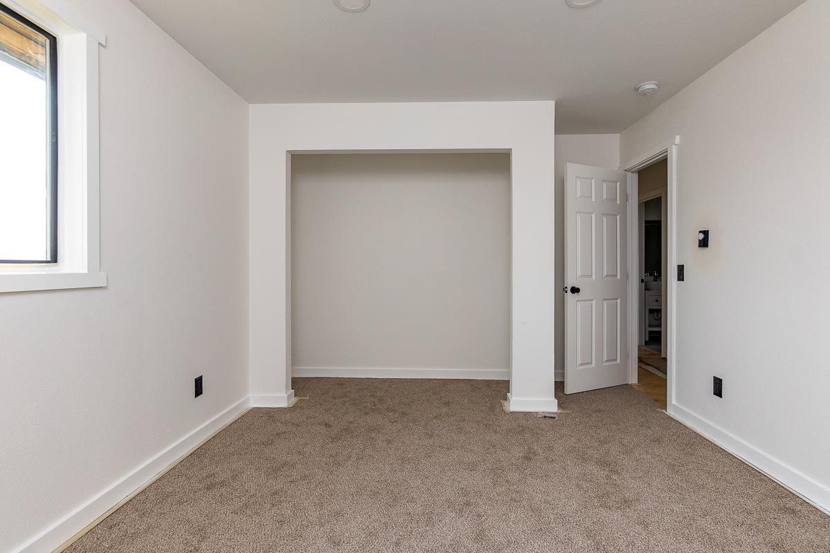 Empty room with carpet, a window, a doorway, and an alcove. White walls and trim.