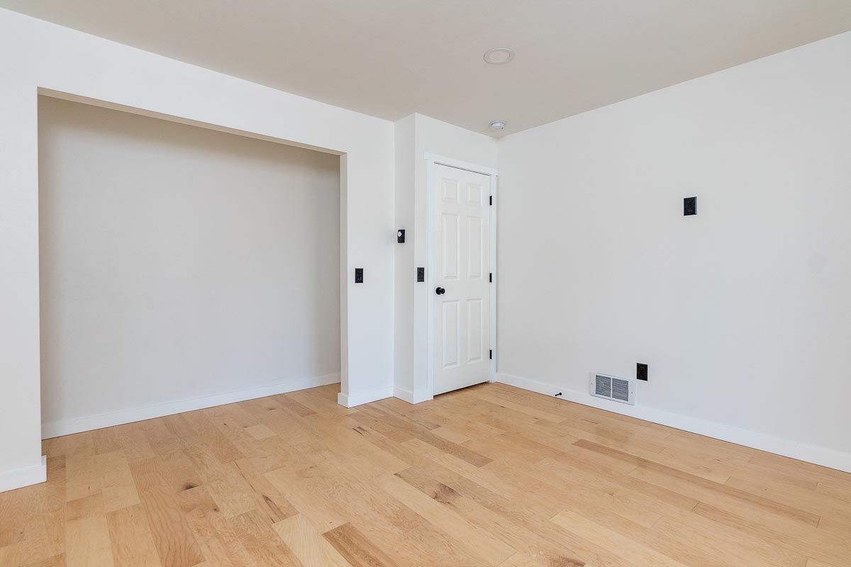 Empty room with light wood floors, white walls, closet, and a closed door.