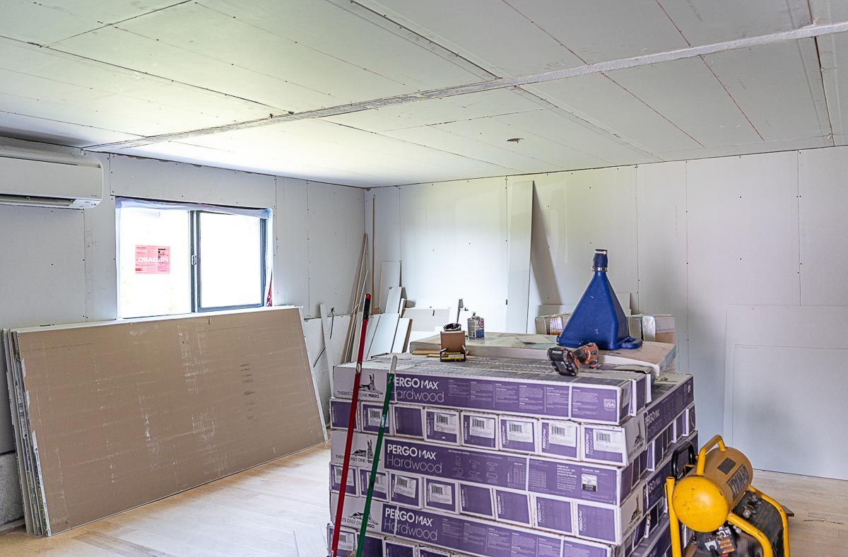Interior of a room under construction, with drywall stacked and leaning against walls and stacked boxes.