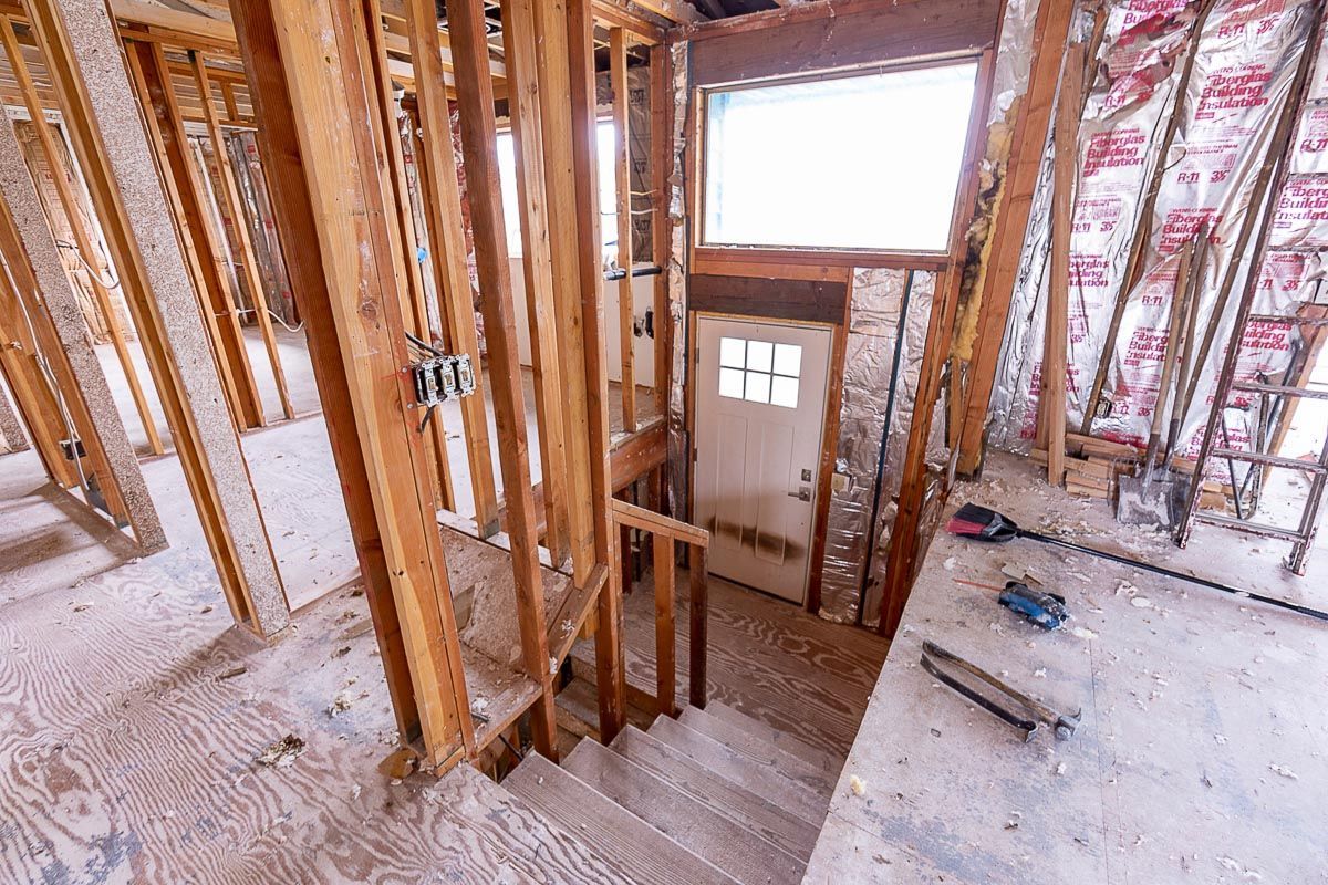 Interior of a home under construction: staircase, wooden framing, open walls, door, and window visible.