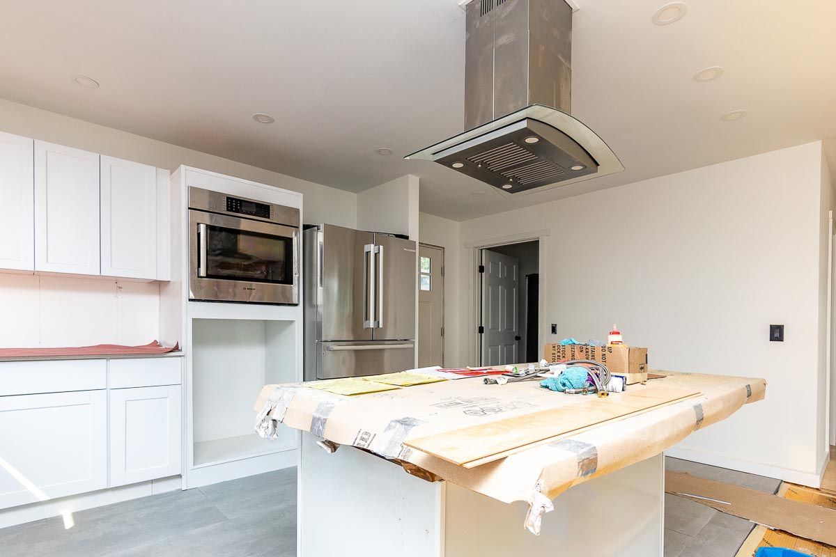 Kitchen with white cabinets, stainless steel appliances, and a central island under construction.