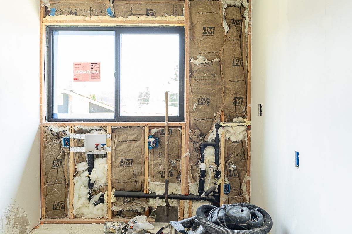 Interior wall under construction with exposed insulation, plumbing, and a window.
