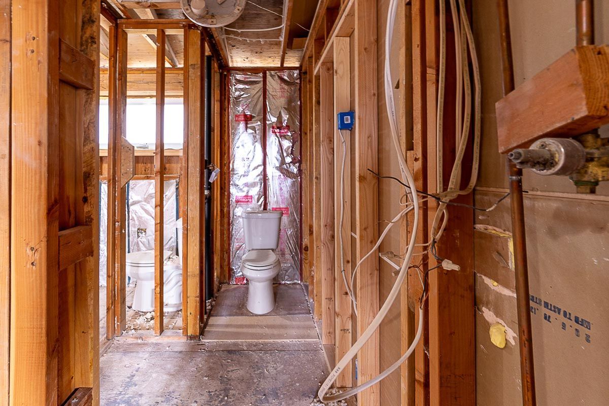 Interior view of a bathroom under construction, showing framing, toilet, plumbing, and electrical wiring.
