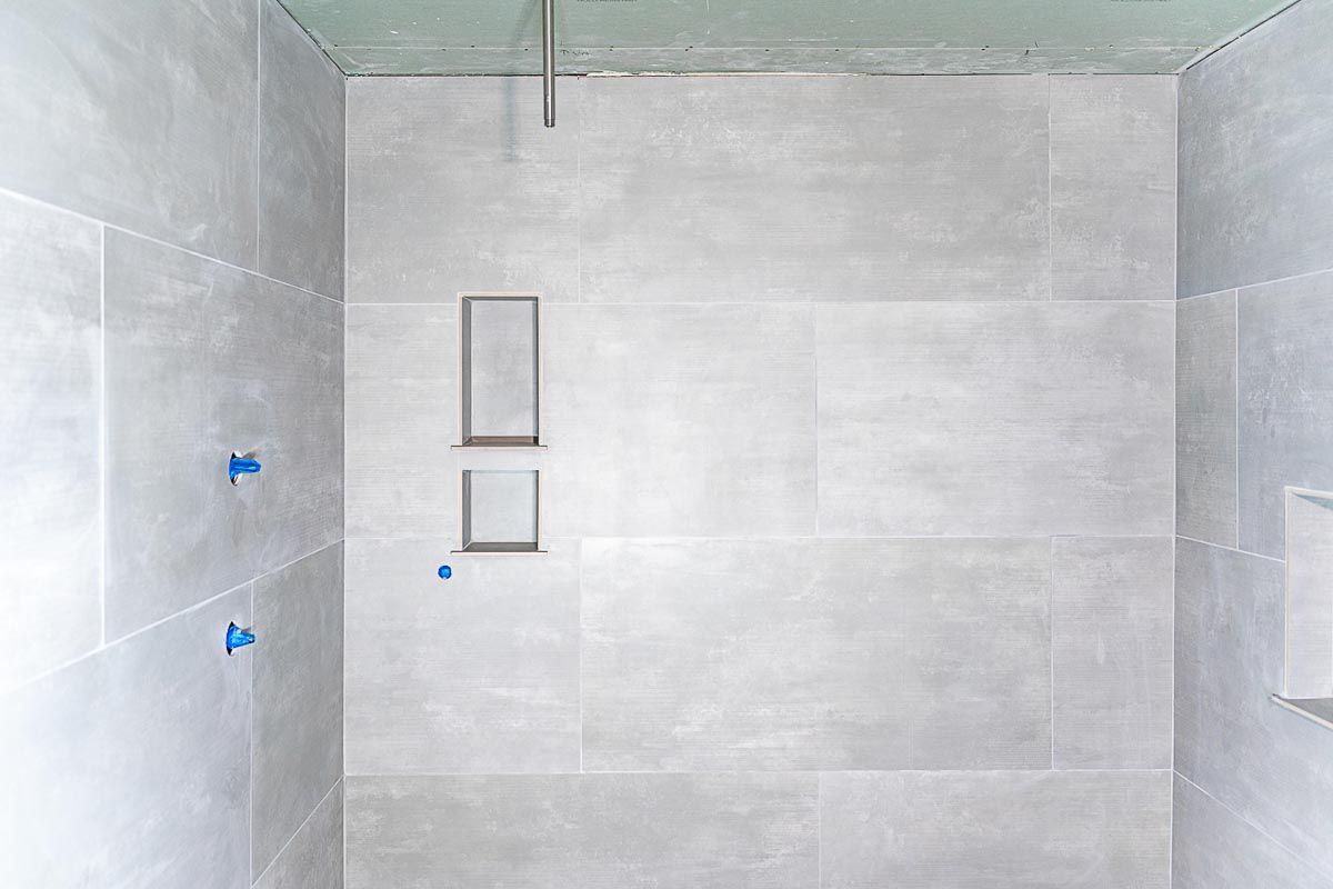 Gray tiled shower with shower head and two recessed niches in a bathroom.