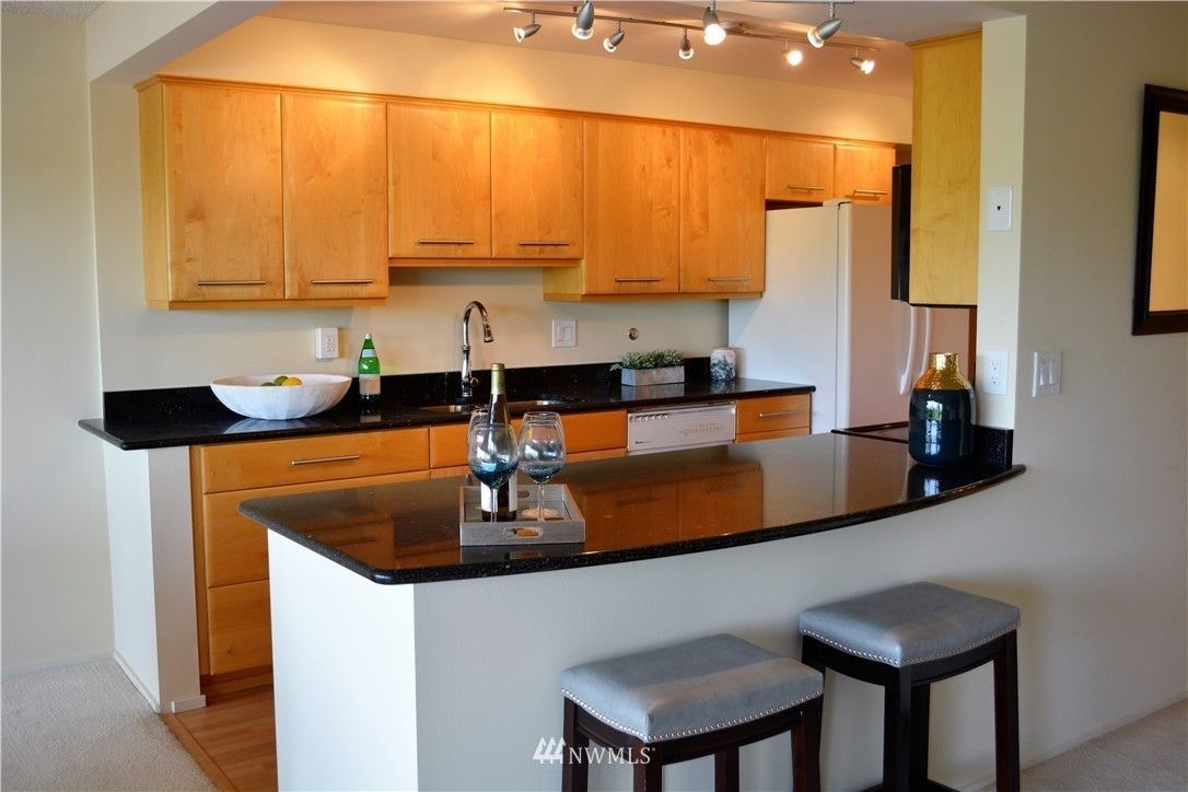 Kitchen with wood cabinets, black countertops, and breakfast bar with stools.