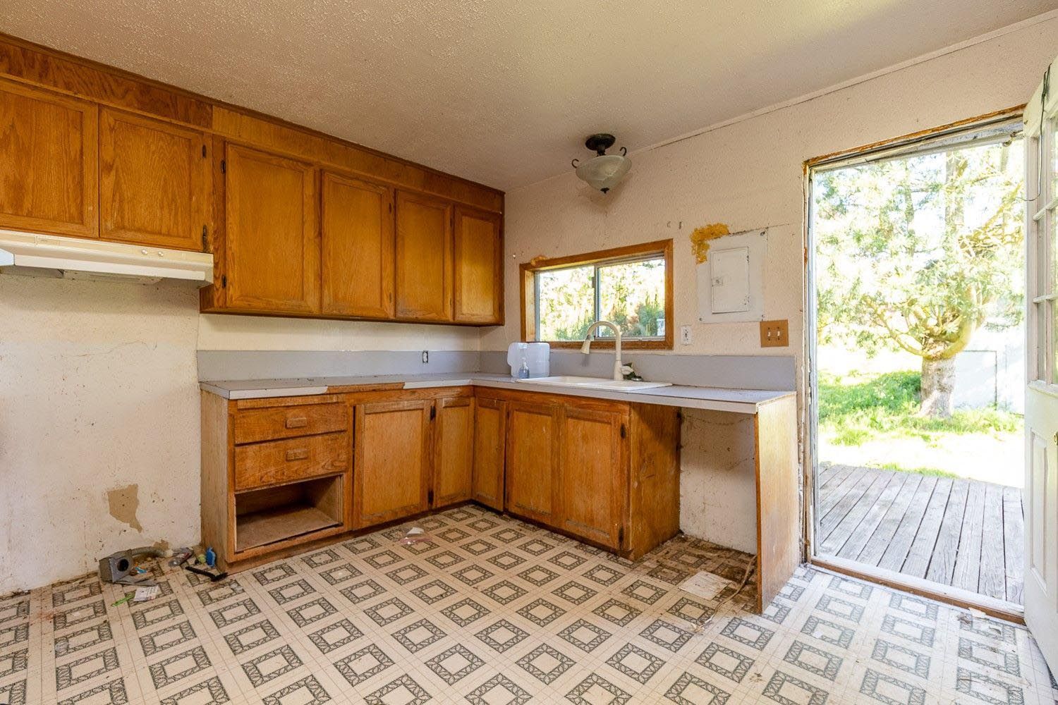 Kitchen with wood cabinets, light countertops, open door to yard, and patterned floor.