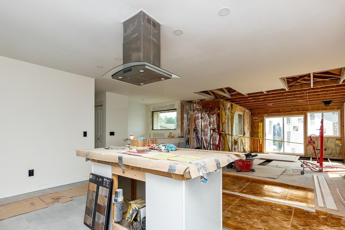 Kitchen under renovation; island with tools, exposed ceiling and walls, range hood, and view to outdoors.