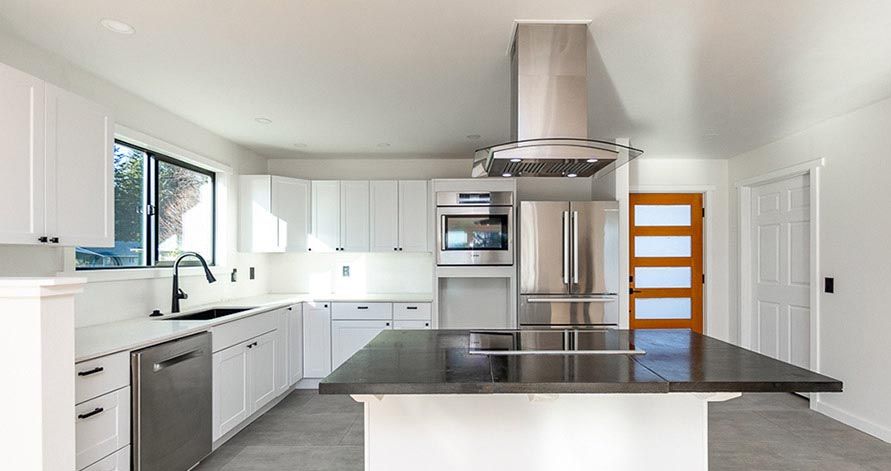 Modern kitchen with white cabinets, stainless steel appliances, dark island, and a light wooden door.