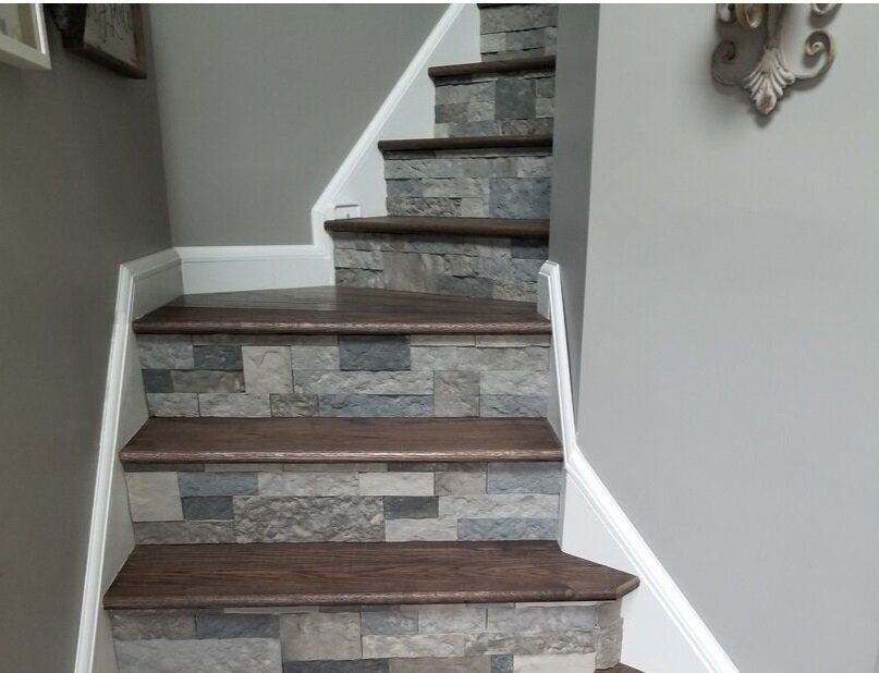 Staircase with wooden steps and stone-look risers. White trim and gray walls.