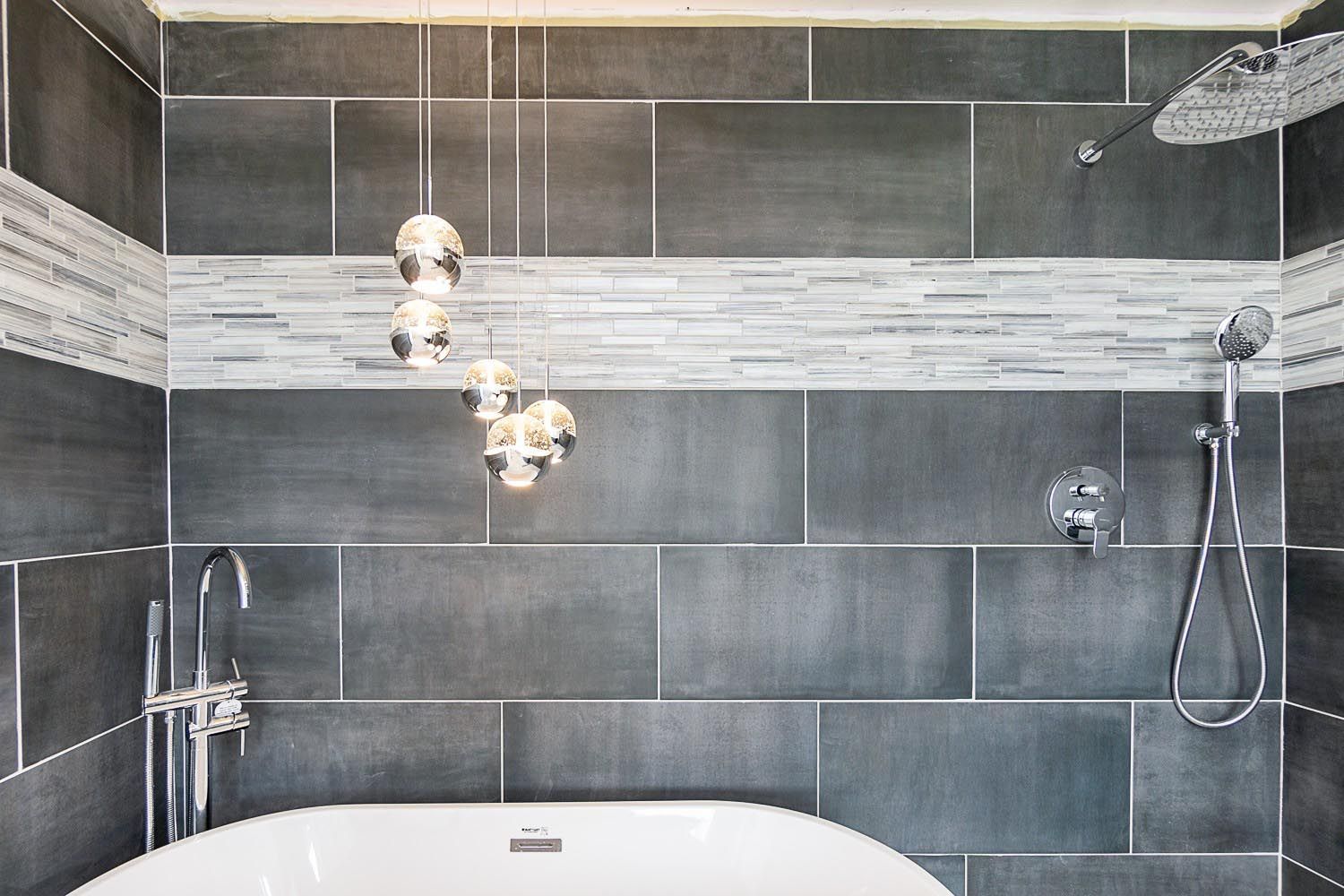 Gray tiled bathroom with white accents and pendant lights.