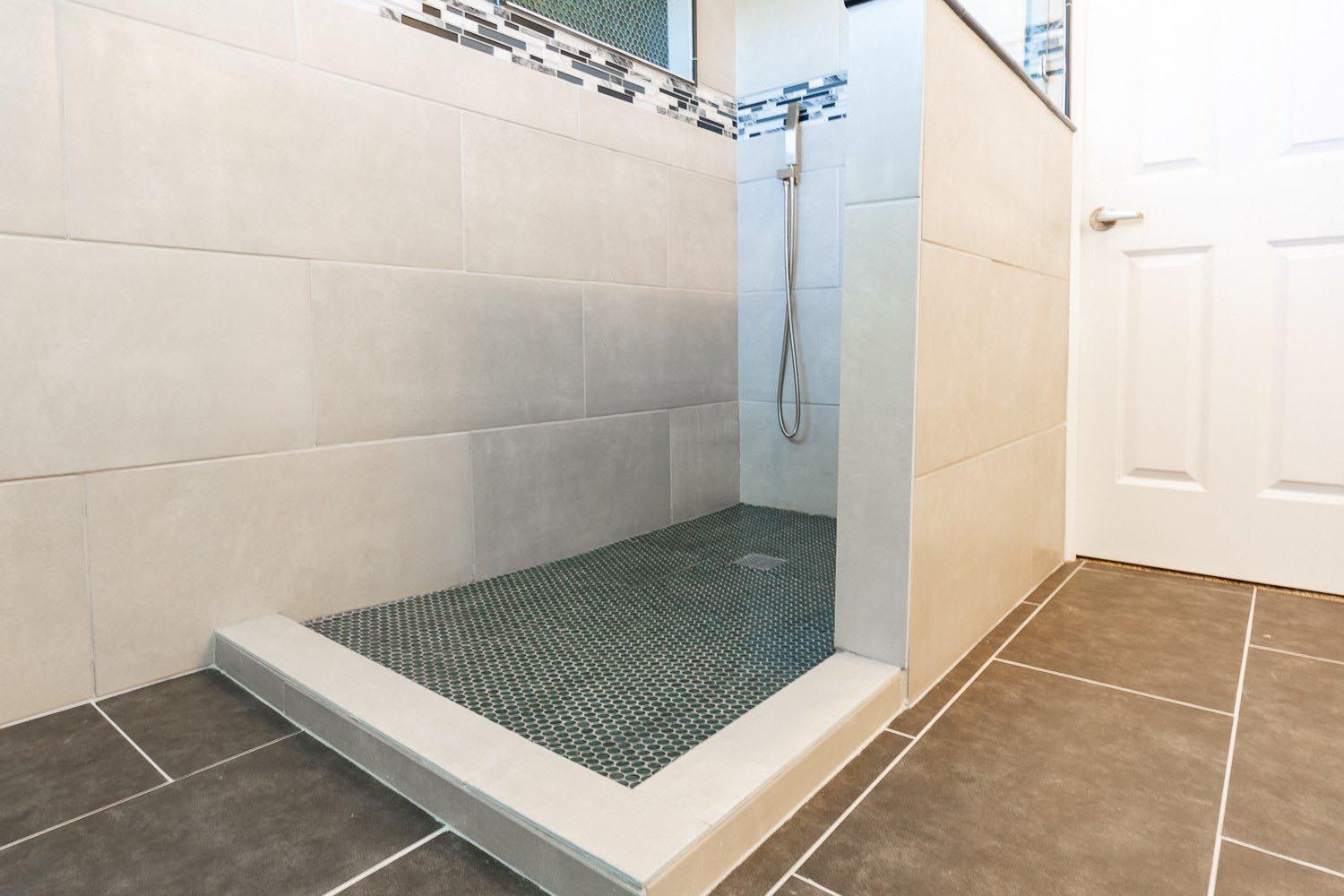 Walk-in shower with gray tile floor, white walls, and a glass-tiled accent.
