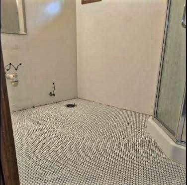 Bathroom with white walls and penny tile flooring. Shower stall is visible on the right.