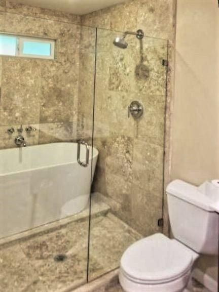Bathroom with a white tub, shower with glass doors, and a toilet. Beige tile walls.