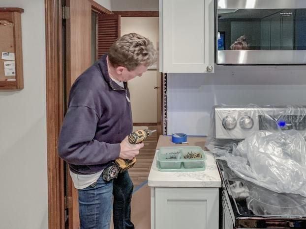 Man using a drill in a kitchen, attaching a shelf bracket.