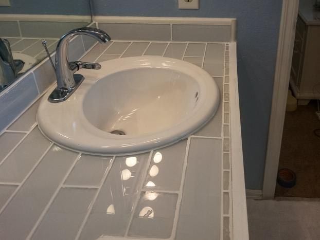 Bathroom vanity with white sink and gray subway tile countertop. Chrome faucet. Blue wall background.