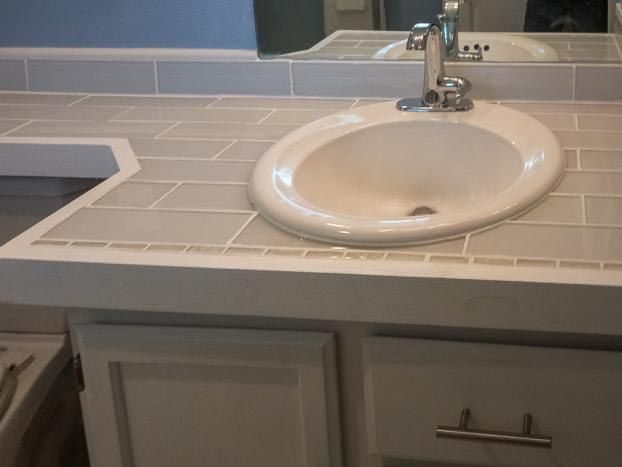 Bathroom vanity with oval sink, light gray tile countertop, white cabinets, and chrome faucet.