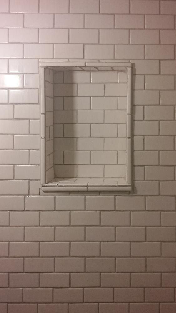 Recessed white tile shower shelf in a white tiled wall.
