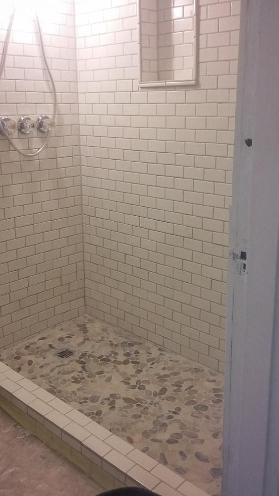 Corner shower with white brick-like tiles, a pebble floor, and glass enclosure.