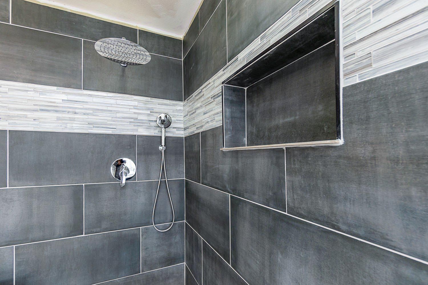 Gray tiled shower with inset shelf and silver fixtures.